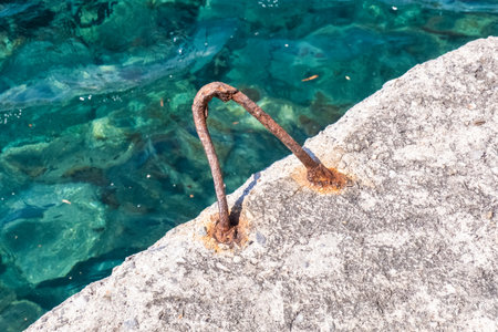 Rusty hook for tying boats on the pier with crystal clear water in the background in Santorini islandの写真素材
