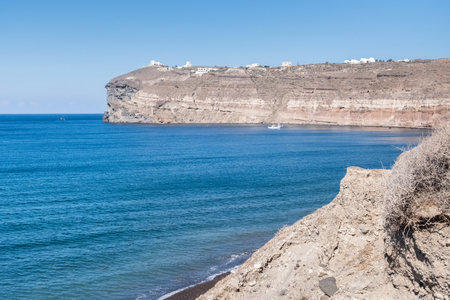 The calm sea of Santorini and a small boat with the rocky wall of the Greek island in the backgroundの写真素材