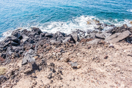 crystal clear sea caresses the dark rocks of the coast of the island of santoriniの写真素材