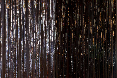 Bright background of tinsel made of metal foil on dark wall. Concept of holiday, fun. Suitable for musical background with space for any lettering or logoの写真素材