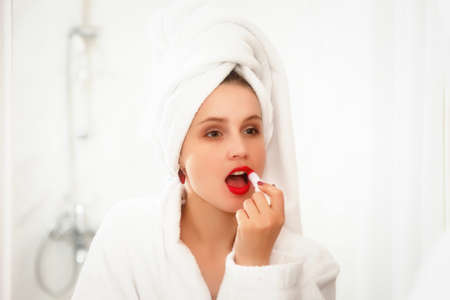 Woman in hotel bathroom after shower. Female of Slavic appearance in dressing gown smiles in mirror. Happy lady looks in mirror. Healthy facial skin. Pretty girl has washed and shows emotionsの写真素材
