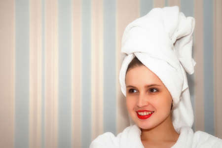 Woman in hotel bathroom after shower. Female of Slavic appearance in dressing gown smiles in mirror. Happy lady looks in mirror. Healthy facial skin. Pretty girl has washed and shows emotionsの写真素材