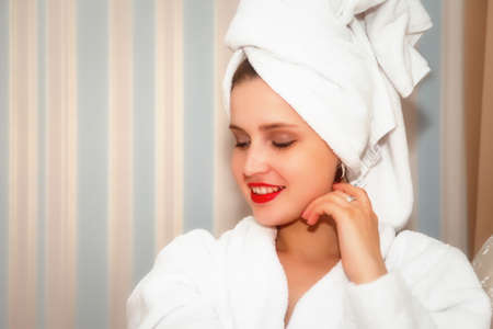 Girl of Slavic appearance in white sexy shirt on bed in a hotel room. Pretty female shows actor's emotions. Young charming woman sitting on sofa in bedroom and playing with her feelings. Relax conceptの写真素材