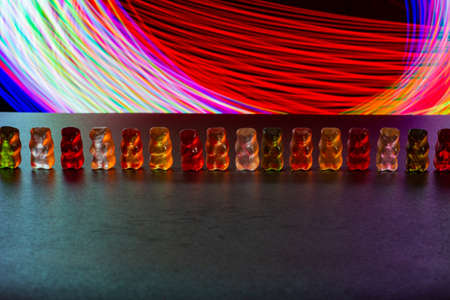 multicolored gelatinous bears stand in a chain against a background of multicolored lights