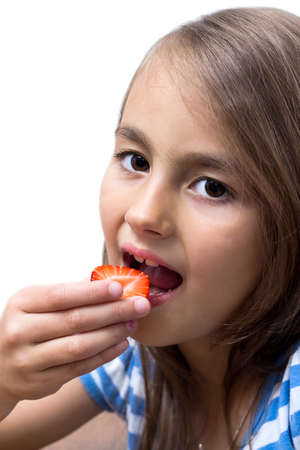 Happy little girl eats strawberries, isolated over whiteの写真素材