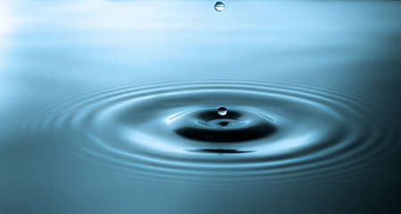 Splash of water crown on blue.Droplet falling in blue water