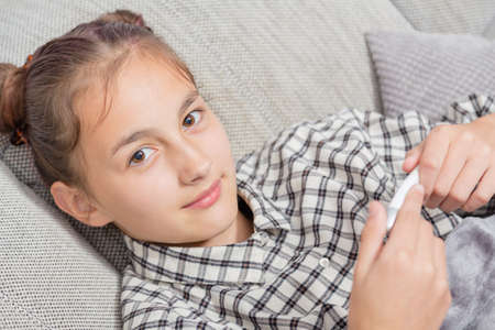 Sick little girl holding thermometer laying in bed with grumpy faceの写真素材