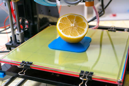 Ripe slice of yellow lemon citrus fruit . 3d printer of the device during the processe.の写真素材