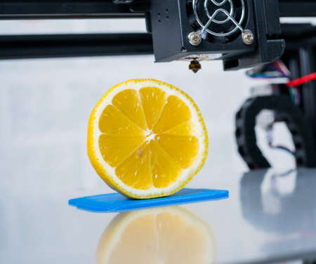 Ripe slice of yellow lemon citrus fruit. 3d printer of the device during the processe.の写真素材