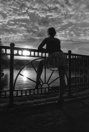 A girl in a short skirt with beautiful long legs watching the sunset. Black and white photography. Attention! The image contains the grain of the photographic film.の写真素材
