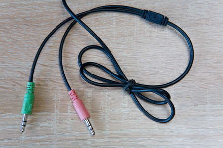 The wires from the headphones with two green and pink plugs lie on a wooden background.