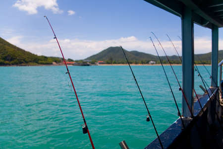 Sea fishing. The fishing rods are leaning against the side of the ship against the background of the hilly coast.の写真素材