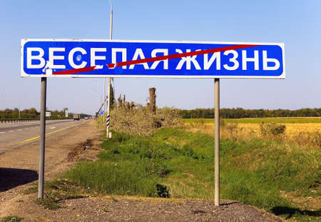 Road sign with a crossed inscription in Russian "Merry life". In the background people cut down the trees .の写真素材