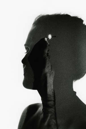 Silhouette of a girl's head and a man's hand with a burning match. Abstract photo. Attention! The image contains granularity and other artifacts of analog photography!の写真素材