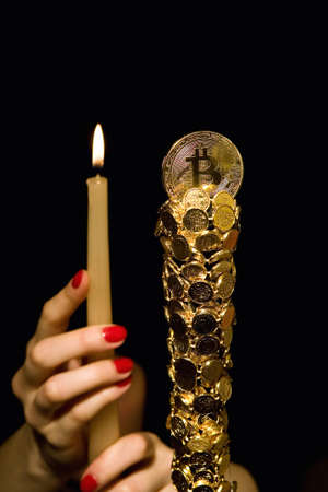 Female hands hold a candle in front of bitcoin. Crypto currency.の写真素材