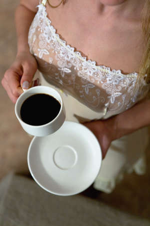 The half-dressed girl in her nightgown is holding a cup of coffee in her hand. View from above.の写真素材