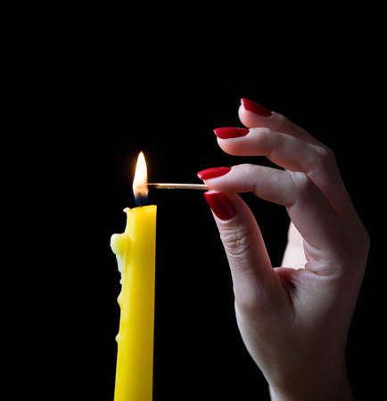 A graceful female hand with a beautiful manicure lights a candle. Close-up.の写真素材