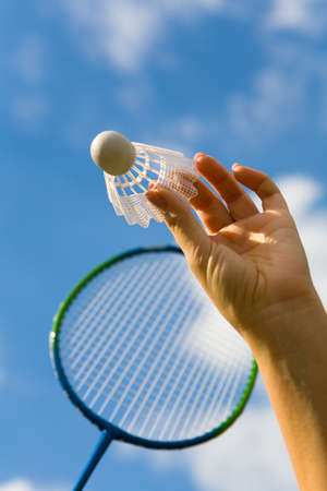 A female hand holds a shuttlecock against the sky. Sport.