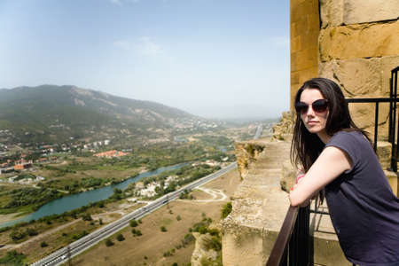 The girl in glasses from the sun against the background of the city of Mtskheta. Georgia.