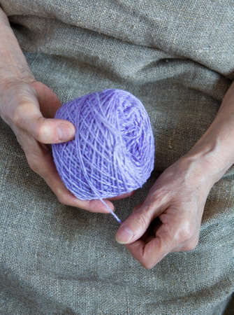 A ball of yarn in the hands of an elderly woman. Close-up.の写真素材