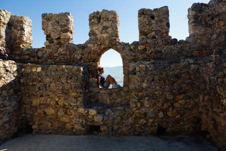 The girl is sitting in the loophole of the fortress wall. Turkey.の写真素材
