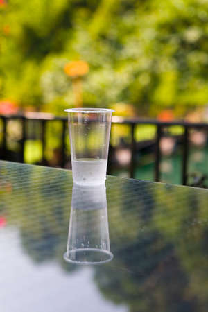 A cheap plastic cup with water is on the table. Outdoors.