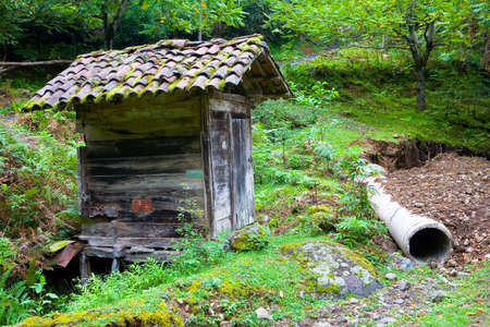 A very small wooden house without windows with a tiled roof. There is a pipe nearby.の写真素材