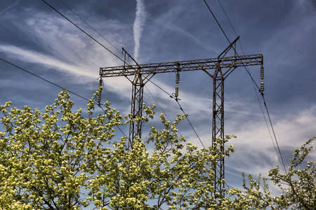 High voltage electric power lines on blue sky with clouds and flowers