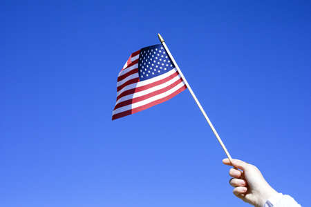 Flag in hand against the blue sky with a copy of space. American flag in hand. Symbol of the holiday, July 4, Independence Day in America.の写真素材