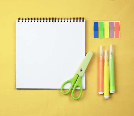White notepad on a yellow background with markers. Yellow background with stationery and a notebook on a spring, School work and learning concept.の写真素材
