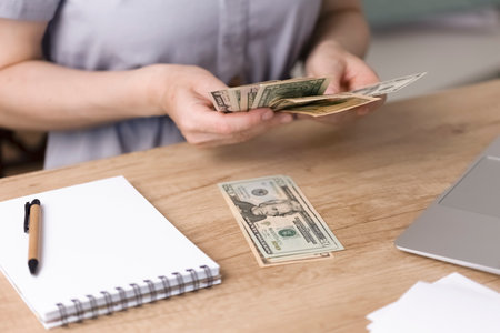 A woman sits at her desk and counts paper money. An accountant or financier counts dollars and...