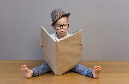 The kid is reading a big book very concentrated. Space for copy. The child sits on the floor with a...