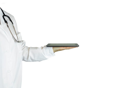 A doctor in a white coat on a white background holds an electronic tablet in his hand. A medical worker with a tablet in his hands, a hospital. A woman doctor in a bathrobe with stethoscopes around her neckの写真素材