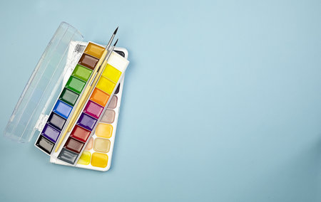 Watercolor paints with brushes on a blue background with copy space. Space for drawing. Back to school. High quality photoの写真素材