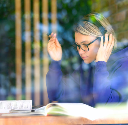 A woman in a cafe at a table with headphones is studying, a student is completing assignments. Young...