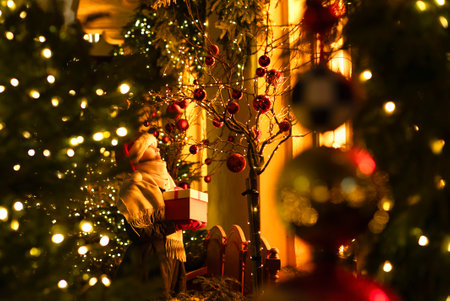 A joyful girl stands in front of a bright shop window with a gift in her hands. Christmas photo, Christmas garland decorated trees and firs, blurred lights, highlights, copy spaceの写真素材