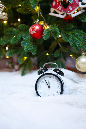 Watch with an alarm clock on a white blanket under a decorated fir. Christmas card with a decorated...