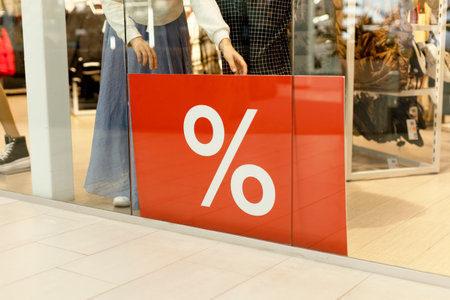 A woman in a store behind a showcase puts a large banner with percentages, Sale, discounts. The seller puts a discount on the goods. Black Friday.の写真素材