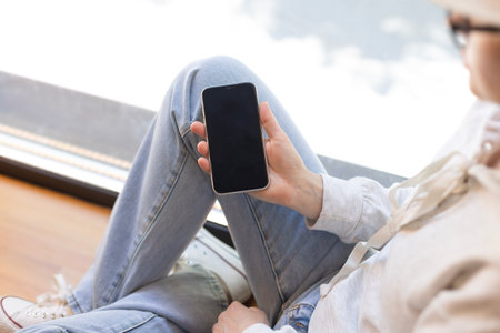 A girl in blue jeans and glasses holds a smartphone in her hand with an empty space. Close-up photo...