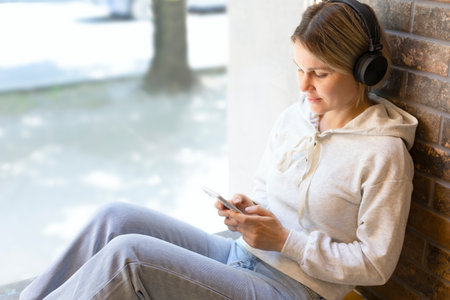 A girl in a gray sweater and headphones with a phone in her hands is writing a message. Beautiful...