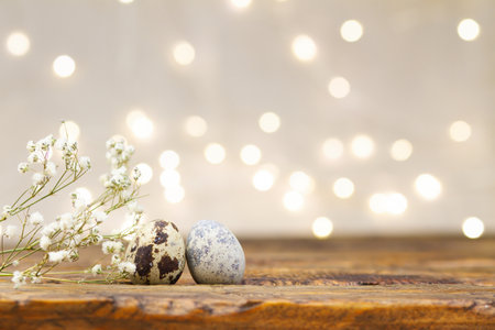 Easter card with quail eggs on wooden table and blurred lights. Beautiful shiny background with...
