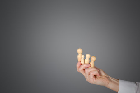 Close-up of a woman's hand on a gray background with wooden figures. Hand with objects isolated on a gray background with space for copying. Woman holding wooden figurines depicting peopleの写真素材