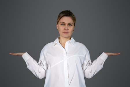 A woman in a white shirt holds her hands at her sides with her palms facing up. Girl isolated on white background with two empty palms for text or objects. Photography for advertising, space for text, copy and advertisingの写真素材