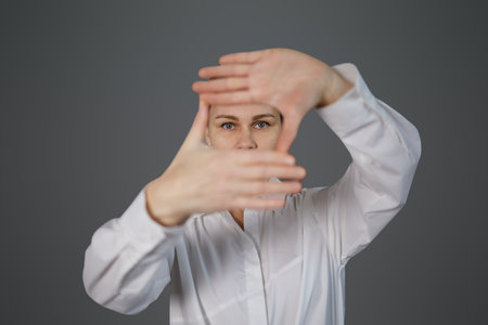 The woman shows her hands only in close-up of her eyes on a gray background. The girl covered her face, leaving only her eyes visible, the woman on the background, space for copy, text and advertisingの写真素材