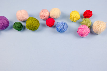 Multi-colored balls of thread are scattered on the table, knitting, embroidery, handwork. Small balls of multi-colored threads on a blue background with space for copy, text and advertisingの写真素材