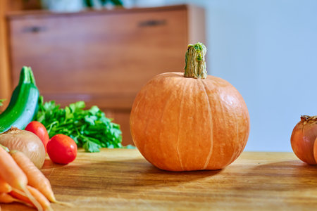 Large orange pumpkin on a wooden board, carrots, tomatoes, herbs for salad. Autumn vegetables on the kitchen table for cooking, dinner or lunch.の写真素材