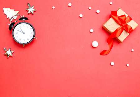 Christmas background with alarm clock, red ribbon gift, toys, snowflakes. Holiday Banner with Christmas Gift on Red Background, Wooden Christmas Tree, Silver Stars, White Snowballsの写真素材