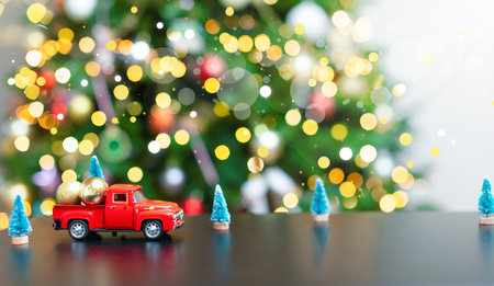 A red little car against the background of a defocus Christmas tree carries golden balls. Christmas background with a red car, blurred lights, small Christmas trees, space for a copy. Holiday cardの写真素材