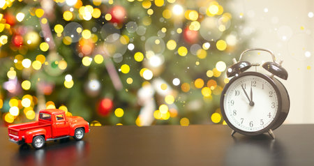 On the wooden board is a red toy car, a New Years clock, blurred lights. Christmas background with...
