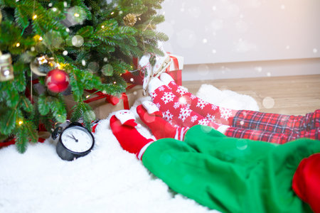 The feet of an adult and a child near the decorated Christmas tree are close-up. Two people sit in front of a decorated spruce tree in red socks. Sit under the tree, celebrate Christmas, New Years hours, holidayの写真素材